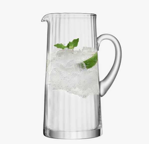 The LSA Aurelia Jug, a classic mouth-blown glass pitcher, is filled with ice, sparkling water, lime wedges, and mint leaves, set against a plain white background.