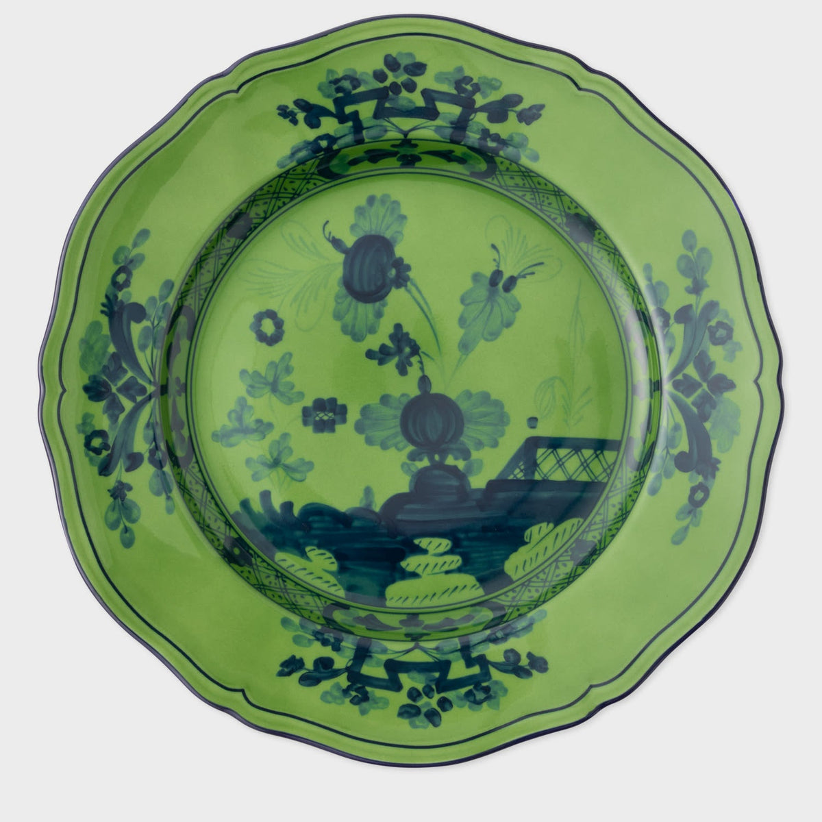 The Oriente Italiano Dinnerware Malachite by Ginori 1735 is a green ceramic plate with a scalloped edge, featuring dark blue floral and oriental-inspired patterns around the rim and center.