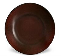 The Terra Wine Dinnerware by L'Objet is a round ceramic plate with a deep reddish-brown hue, darker at the rim and lighter in the center, set against a white background.