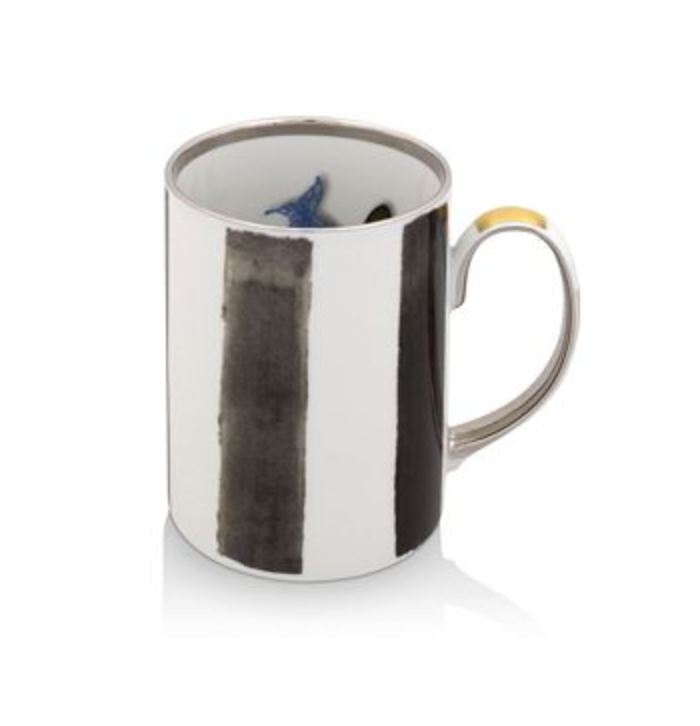 The Sol Y Sombra mug by Christian Lacroix x Vista Alegre features vertical black brushstroke stripes on white ceramic, a metallic silver handle with a gold accent, and a blue design inside—echoing the brand's signature artistry.