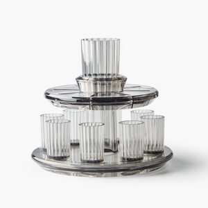 The Apeloig Kiddush Wine Fountain Set features eight ribbed clear glasses on a two-tiered fountain with a central Kiddush Cup, all crafted from transparent material—an elegant addition to your Judaica collection.