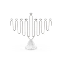 The Coluna Menorah Carrara Marble & Silver by Anna New York features a striking geometric, wavy design with eight silver branches set atop a smooth Italian Carrara marble base. Photographed against a plain white background, this modern menorah seamlessly blends contemporary style with timeless elegance.