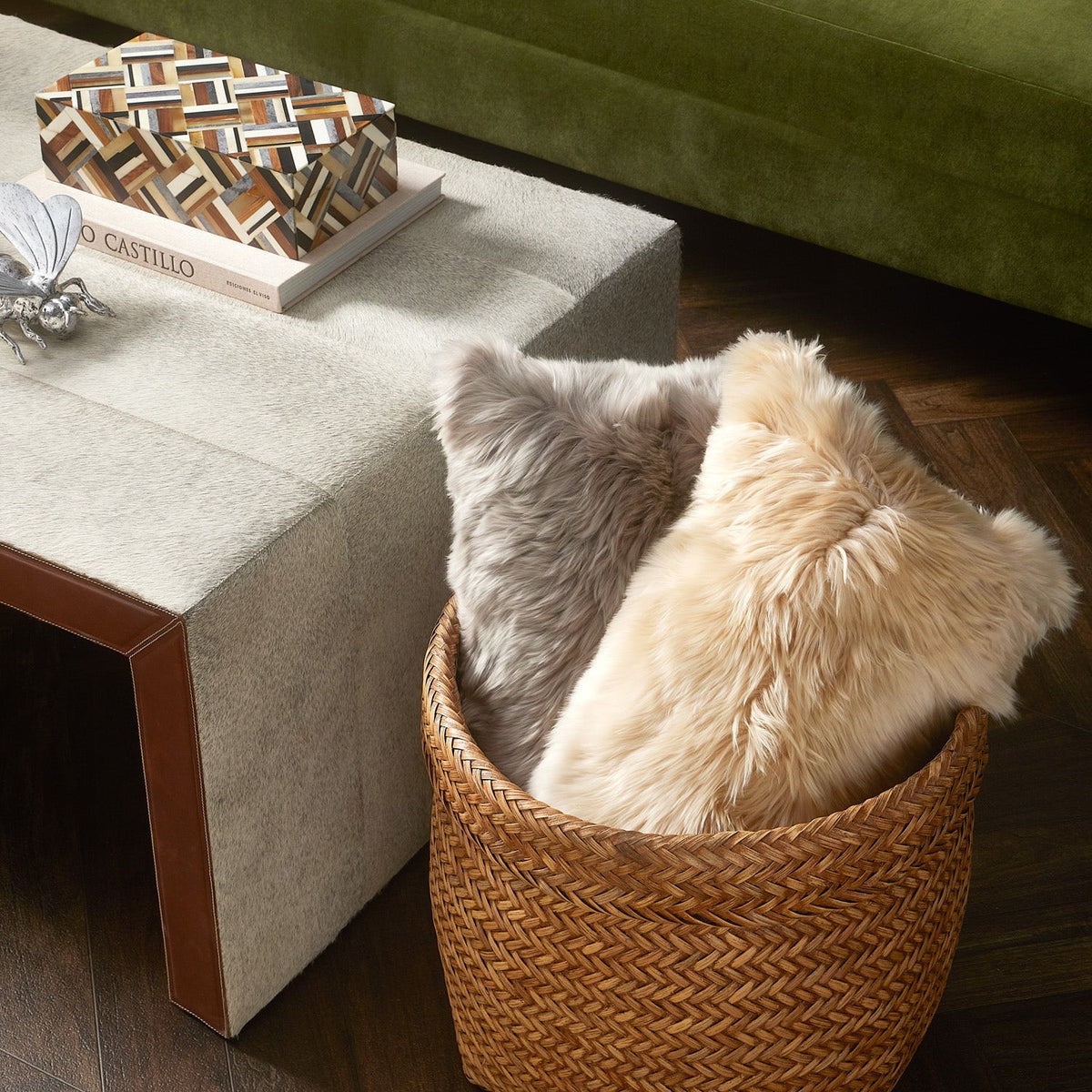 A Hunter Horn Box with geometric wood and horn inlay rests on a coffee table beside a basket filled with two fluffy faux-fur pillows.
