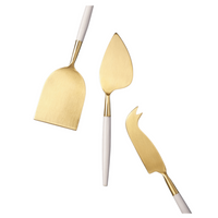 The Be Home White & Gold Cheese Set features three gold knives with white handles—a flat chisel, pointed knife, and fork-tipped knife—arranged on a white background for a stylish, unique finish to your home essentials.