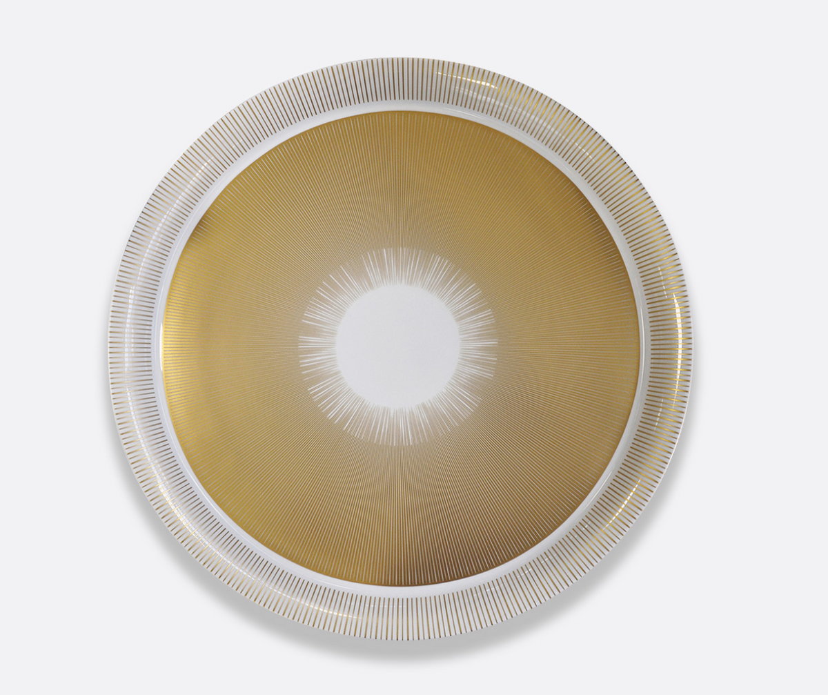 The Sol Dinnerware by Bernardaud features a round design inspired by Limoges porcelain, with a golden center, fine white lines forming a sunburst, and a sleek white and silver rim with linear patterns.