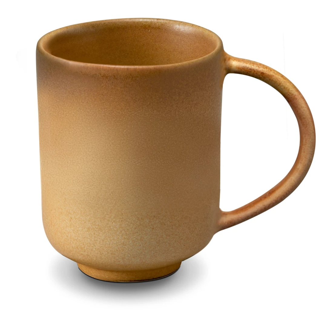 The L'Objet Terra Leather Dinnerware ceramic mug features a matte, speckled light brown finish and large rounded handle, recalling hand-crafted style, shown on a white background.