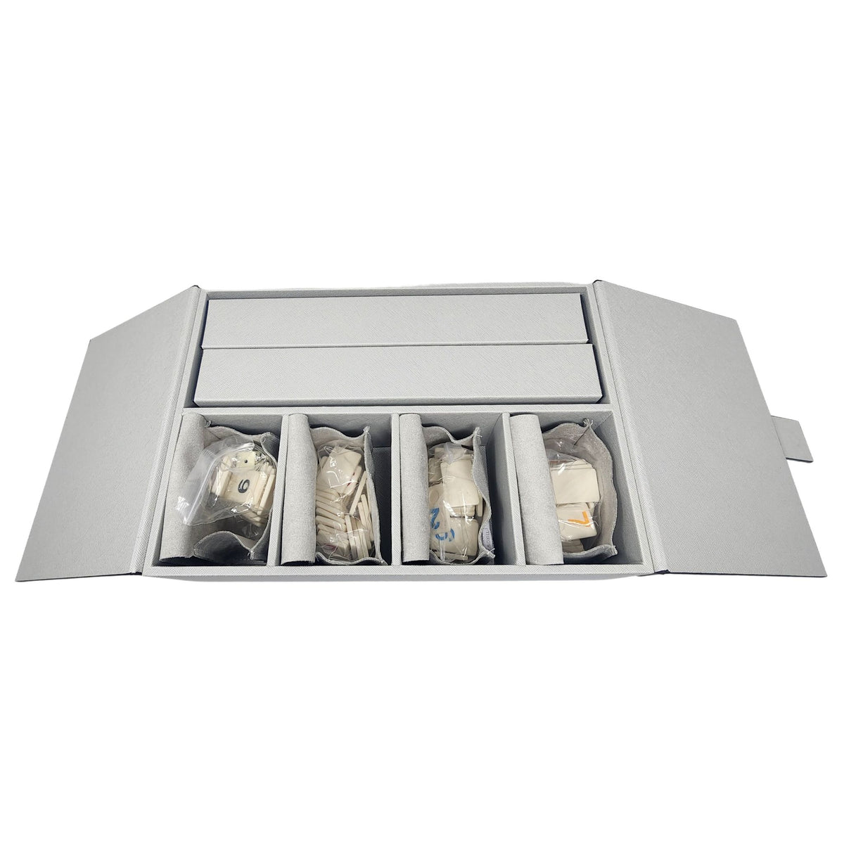 The Excelsior Rummikub Set Silver by Brouk & Co features a gray, textured leather box with open flaps, revealing four compartments inside—each holding a beige collectible tile wrapped in clear plastic for a unique game set addition.
