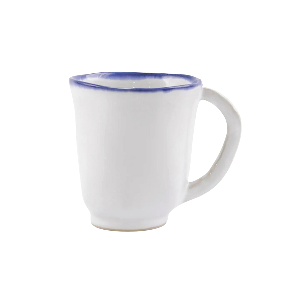 The Vietri Aurora Edge Dinnerware mug is handmade in Italy from white stoneware, features a curved handle and blue rim, is chip resistant, and is shown against a plain white background.