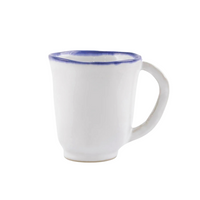 The Vietri Aurora Edge Dinnerware mug is handmade in Italy from white stoneware, features a curved handle and blue rim, is chip resistant, and is shown against a plain white background.