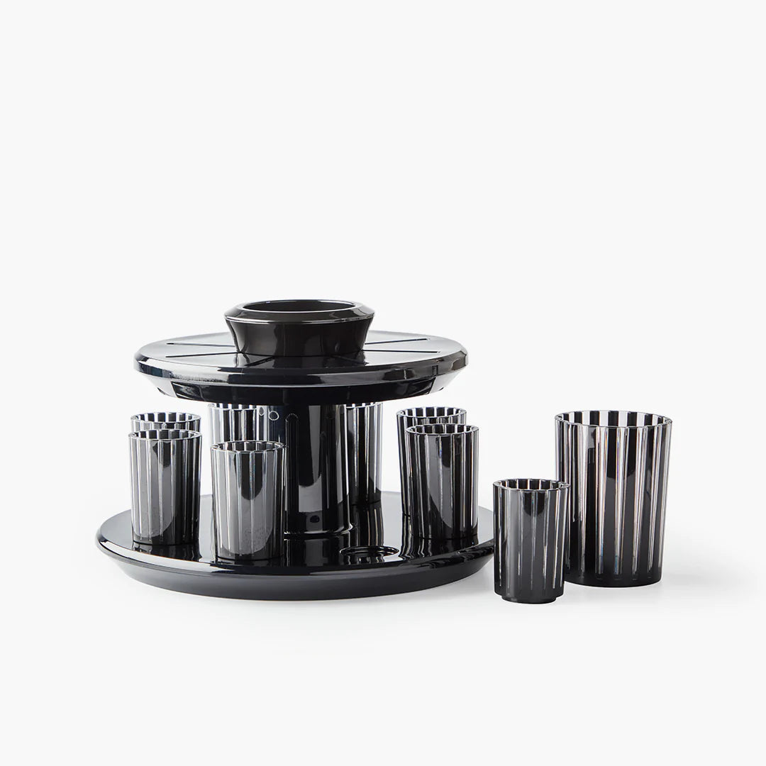The Apeloig Kiddush Wine Fountain Set features sleek black and clear striped glasses around a matching circular tray and central holder, blending modern Judaica design with a glossy finish for stylish wine serving.
