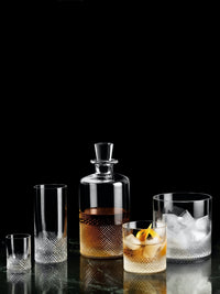 The Richard Brendon Diamond Shot Glass Set of 2 features elegant hand-cut crystal glasses displayed on a dark surface, with one glass containing an amber liquid, all set against a striking black background.