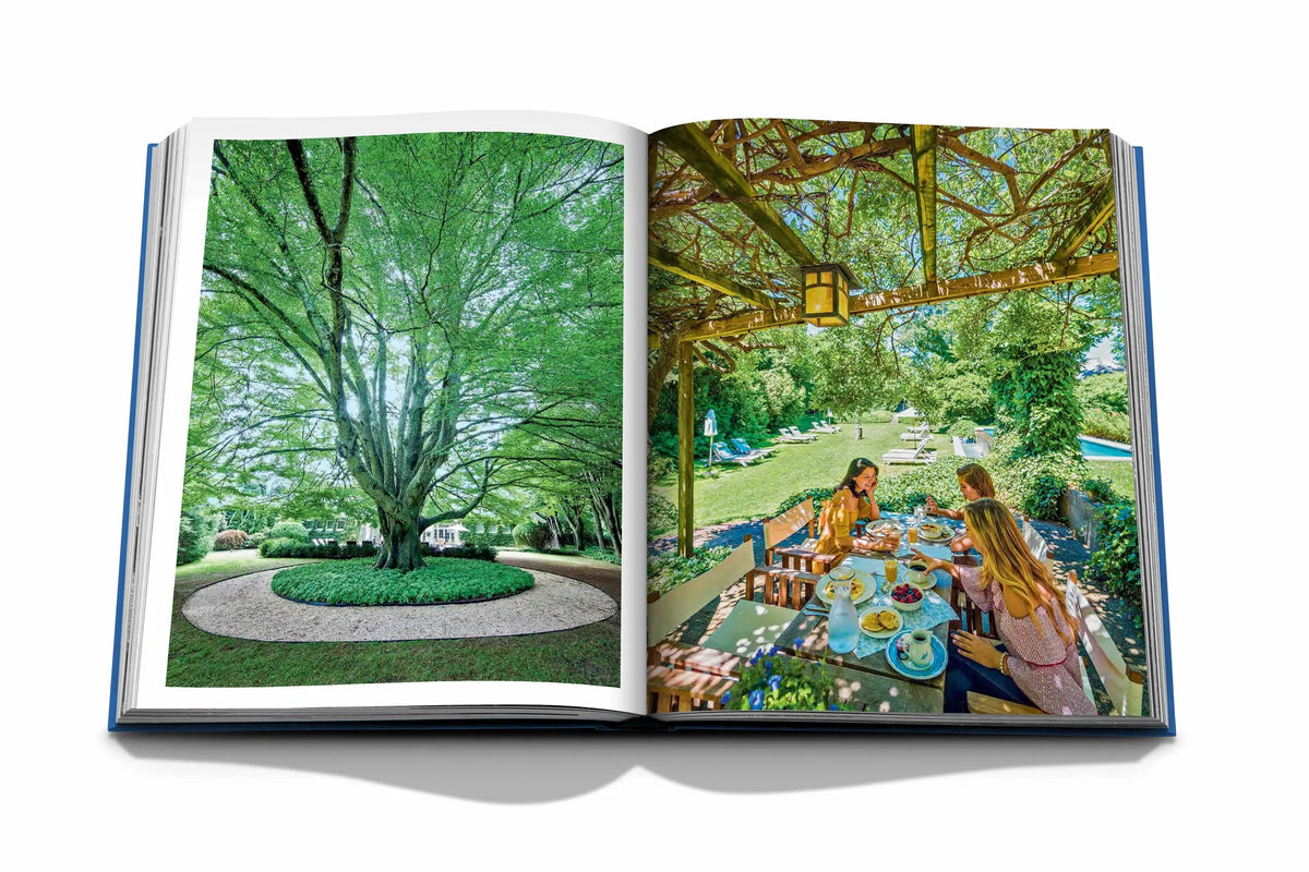 The Hamptons Private by Assouline features an open book with a leafy tree on one page and people dining outdoors under a pergola on the other, capturing a summer vacation vibe inspired by The Hamptons.