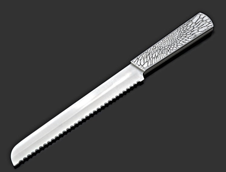 The Organic Lace Challah Knife Silver by Metalace Art features a serrated, shiny blade and a metal lace-patterned handle—an elegant piece displayed on dark gray, perfect as a memorable wedding gift.