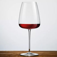 A Luigi Bormioli Talismano Bar Collection Set wine glass with a thin stem rests on a wooden surface, partially filled with red wine, against a plain light grey background, showcasing elegant Italian craftsmanship.