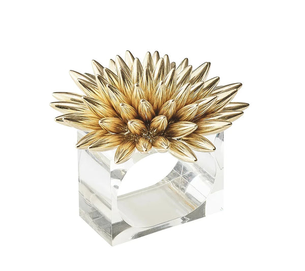 The Stellar Napkin Ring Gold Set of 4 by Kim Seybert features a clear rectangular Lucite design topped with a large gold flower, its spiky petals arranged in a striking circular pattern.
