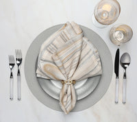 Elegant table setting features a gray and white plate, striped napkin with a gold ring, cutlery, and glasses—all arranged on the Kim Seybert Shagreen Placemat Elephant Grey Set of 4 atop a white surface.