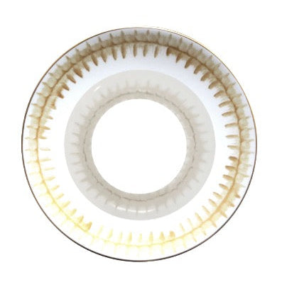 The lens resembles Marie Daâge Rafia 5 Dinnerware by Marie Daâge, with a circular pattern, dark brown outer ring, and lighter brown/yellow gradient at the center. It’s shown singly against a white background.