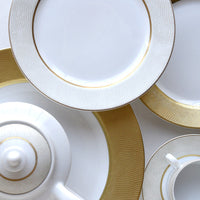 A close-up of Bernardaud’s Sauvage Gold Dinnerware—plates, teapot, and cup—features elegant gold textured rims and subtle embossed snakeskin detail, all arranged in an overlapping display.