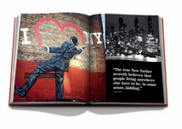 Assouline’s "New York By New York" book showcases iconic images—a man in a suit before an I ❤️ NY mural and a black-and-white city skyline with a quote—beautifully presented in a luxury slipcase.