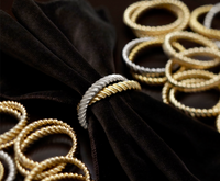 The Deco Twist Napkin Ring Set of 4 by L'Objet features twisted 24K gold-plated rings, shown holding a black velvet napkin on a dark surface—a luxurious gift, beautifully boxed.