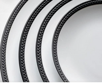 Three Soie Tressée Black porcelain plates by L'Objet, featuring dark, braided-style rims and textured edges, are arranged diagonally on a light background, creating a striking visual motif.