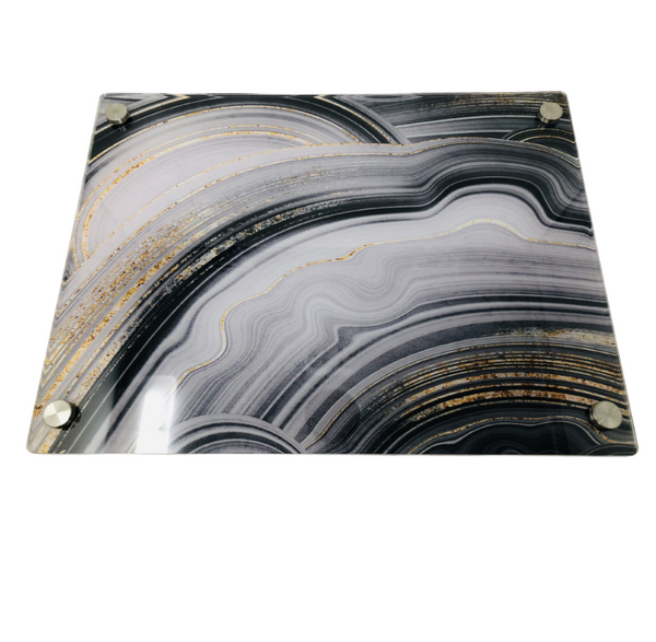 The Eye Candy Raised Black Slice Challah Serving Board features a black, white, and gold marbled glass design with four round metal feet—perfect as a stylish challah board or an elegant sushi platter.