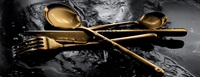 The Mepra Linea 5 Piece Setting - Oro flatware is arranged in a crisscross pattern on a dark, textured surface with water droplets.