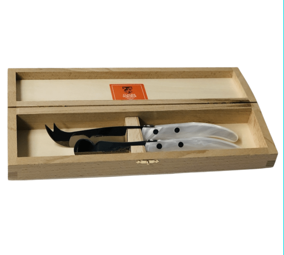 The "ULTIMATE" Berlingot Cheese Set White by Claude Dozorme features two curved stainless steel knives with translucent handles, beautifully displayed side by side in an heirloom-quality wooden box.