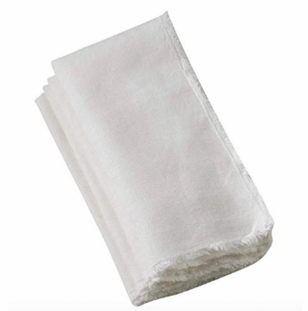 A folded Saro Trading Fringed Stone Washed Napkin in ivory, with subtly frayed edges, is displayed on a plain white background. Set includes 4 napkins.