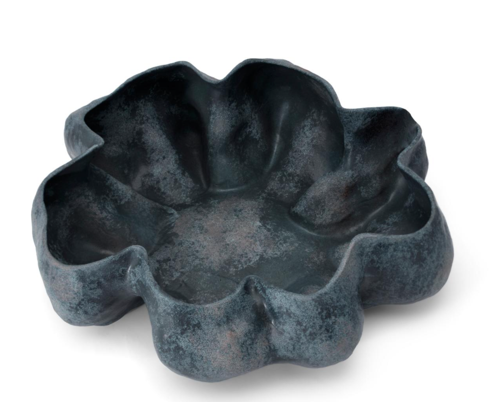 A dark blue, textured bowl shaped like a flower with six large petals, reminiscent of handmade porcelain, the Timna Bowl Blue by L’Objet is set against a white background.