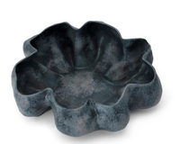 A dark blue, textured bowl shaped like a flower with six large petals, reminiscent of handmade porcelain, the Timna Bowl Blue by L’Objet is set against a white background.