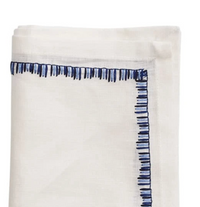 The Kim Seybert Filament Napkin White & Navy Set of 4 features neatly folded white linen napkins with uneven navy blue stitched lines along the edge, adding an embroidered look to your table setting.