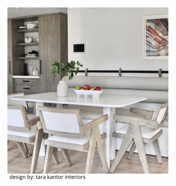 A modern dining area with a white table, light wood and white chairs, a built-in bench, and a decorative centerpiece. Open shelves, the FS Objects Standing Bowl Oval, and framed abstract art accent the minimalist space. Design by Tara Kantor Interiors.
