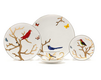 The Bernardaud Aux Oiseaux Dinnerware set features white Limoges porcelain adorned with gold branches, colorful birds, and butterflies. The set includes three plates in various sizes plus a teacup and saucer.
