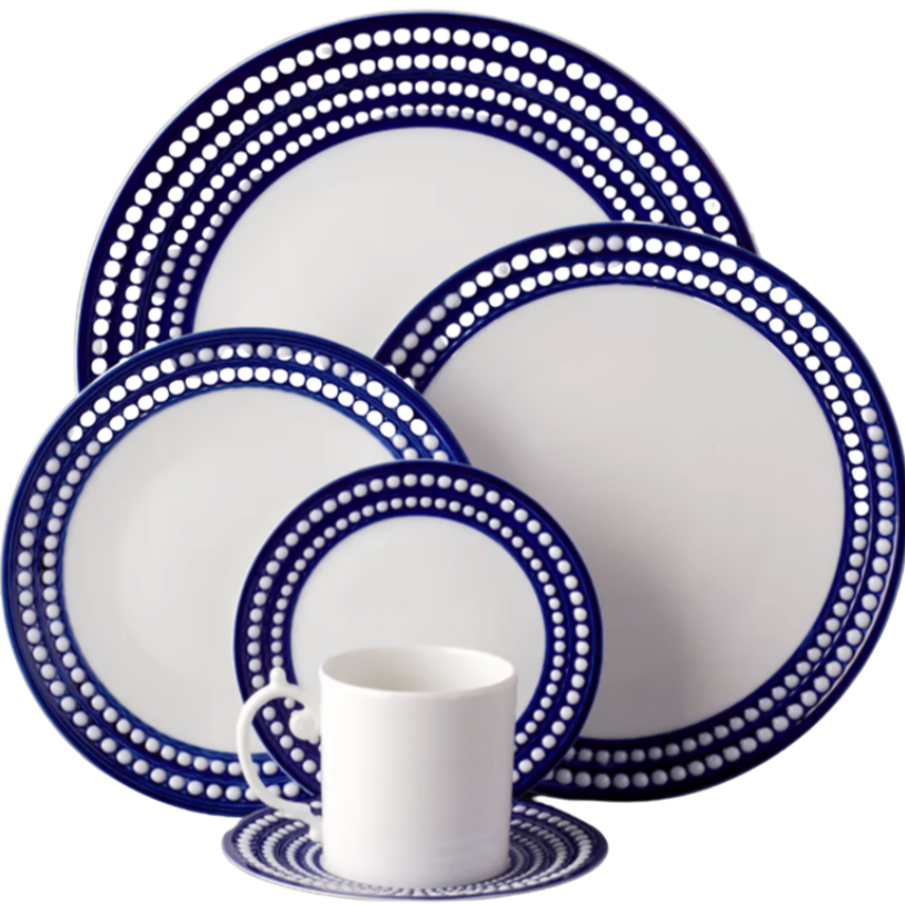 The Perlèe Blue Dinnerware by L'Objet features Limoges porcelain plates, bowl, cup, and saucer with a circular dot pattern on white and dark blue edges from the L’Objet Perlèe Collection.