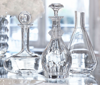 Three Baccarat Chateau Decanters are elegantly displayed on a reflective surface, illuminated by soft natural light. Each decanter showcases a distinct shape and intricate design, highlighting Baccarat’s renowned craftsmanship.