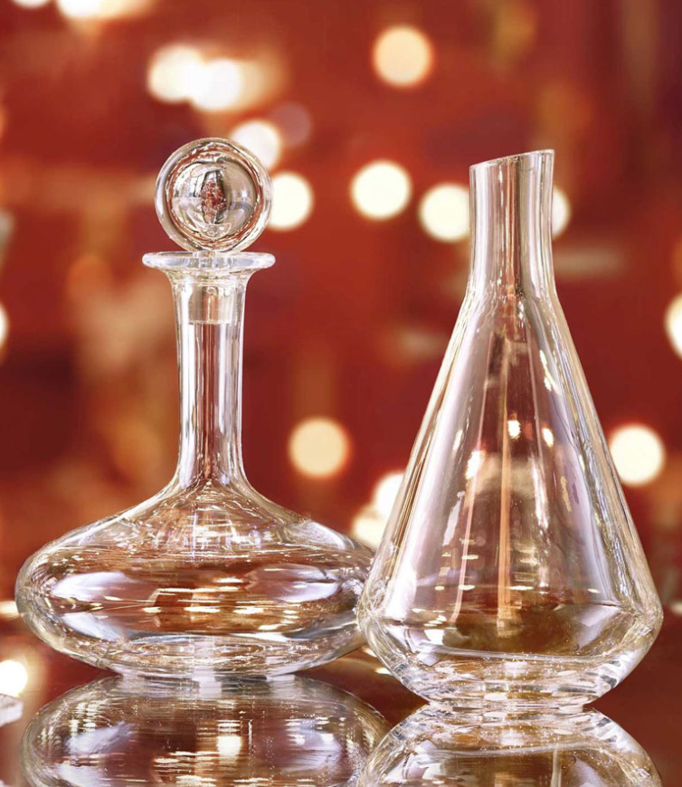 Two empty Baccarat Chateau Decanters are side by side on a reflective surface, with warm, blurred lights in the background for a festive atmosphere.