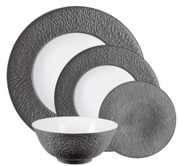 The Raynaud Mineral Irise Dinnerware Dark Grey set features textured dark gray exteriors and smooth white interiors. Made in France, it includes two plates, one smaller plate, and a bowl, all displayed overlapping each other.