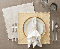 Two square Stamped Reversible Placemat Silver & Gold placemats with scalloped edges arranged on a table with a place setting of plates, a napkin in a ring, flatware, and two glasses.