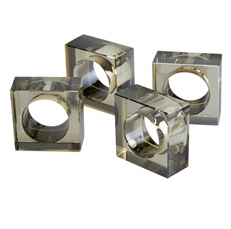 The Tizo Crystal Cube Napkin Ring Smoke Set of 4 features square, transparent rings with circular cutouts—perfect for adding a modern touch to stylish table settings.
