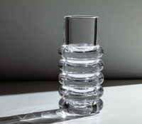 The Tom Dixon Press Stem Vase, by Tom Dixon, features clear cylindrical glass with four rounded ridges and sits on a flat surface, casting a soft shadow in diffused light for a modern look.