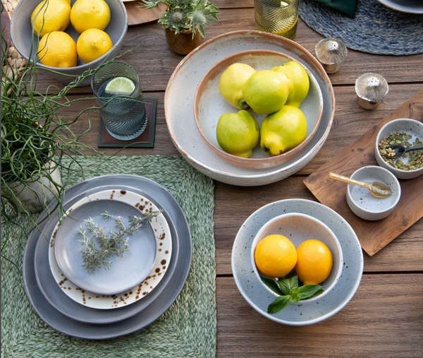 A rustic table set with the Marcus Cement Dinnerware Set of 4 by Blue Pheasant, filled with citrus, herbs, and spices on green woven placemats, creates a fresh and natural look.