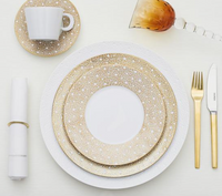 Elegant table setting with Bernardaud Ecume Dinnerware Mordore porcelain plate with gold-dotted rims, a white cup and saucer, gold and white napkin with gold ring, gold fork and knife, and an amber wine glass.