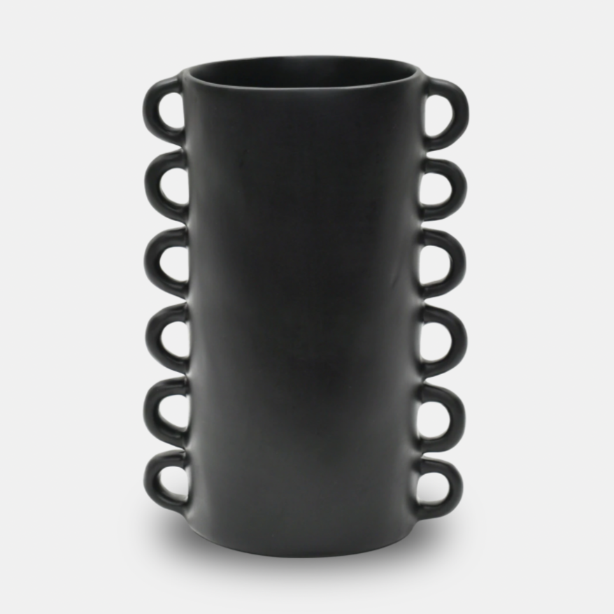 The Tina Frey Loopy Resin Vase Black is a tall, cylindrical vase with a matte finish and six evenly spaced loop handles on each side, shown against a plain white background.