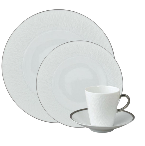 The Raynaud Mineral Irise Dinnerware Platinum set features elegant white Limoges porcelain with a subtle texture and platinum trim, including a dinner plate, salad plate, bread plate, and teacup with saucer.