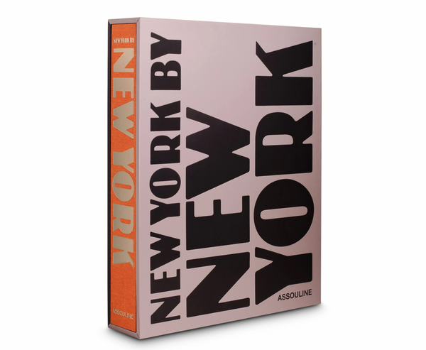 A large hardcover photography book, "New York By New York" by Assouline, features bold black text on a light pink cover with an orange spine. The book stands upright and is slightly angled to the right.