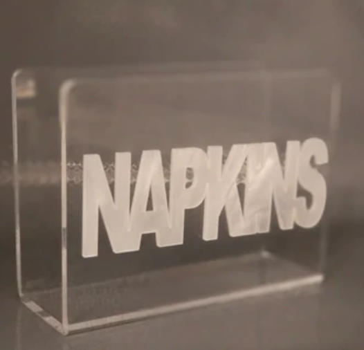 The Eye Candy Acrylic Napkin Holder features a modern clear design with "NAPKINS" in bold, white letters across the front.