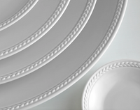 Close-up of four Soie Tressée White Dinnerware plates by L'Objet, each featuring a braided pattern along the rim and crafted from elegant Limoges porcelain, arranged in an overlapping display on a light surface.