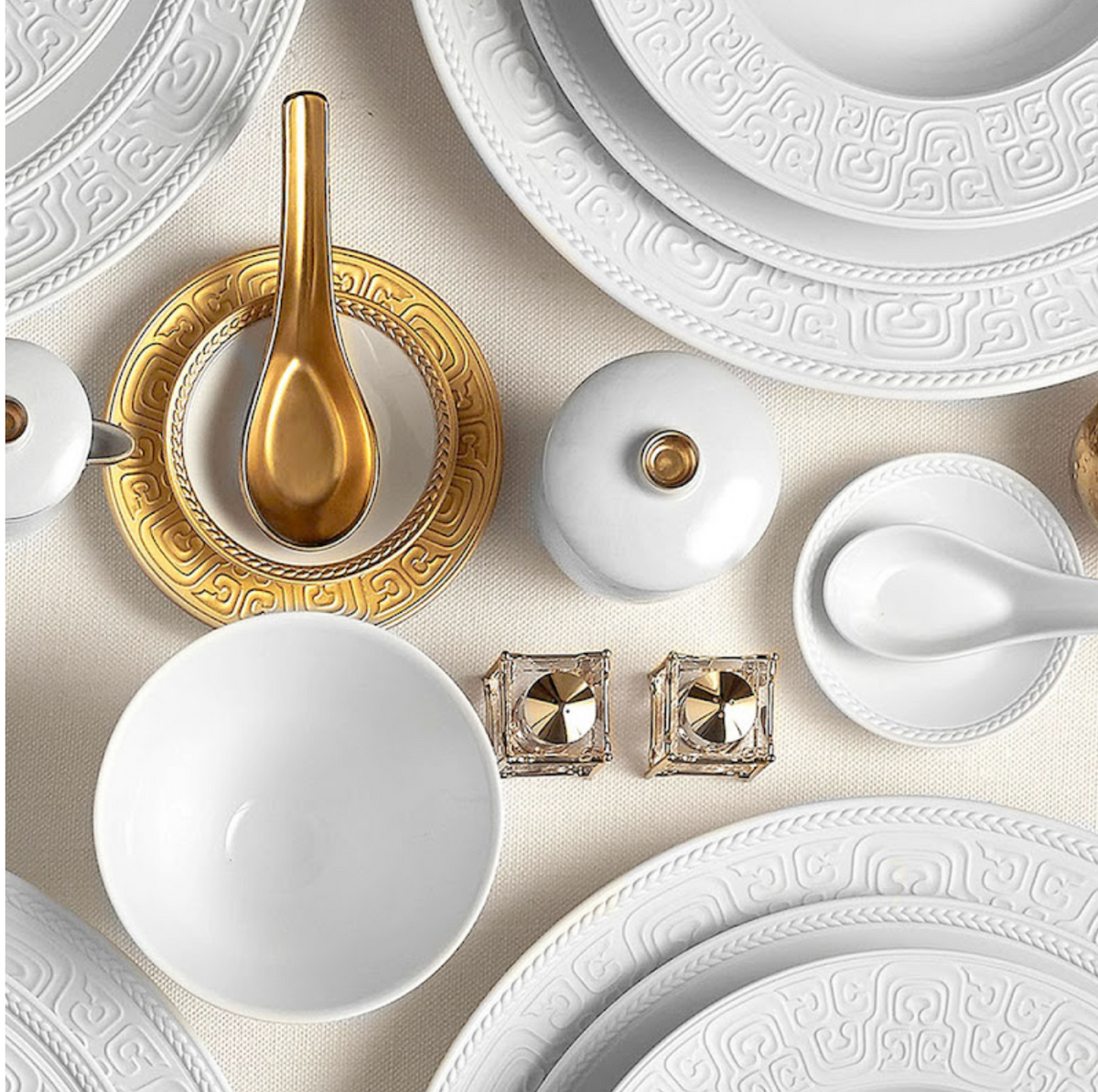 L'Objet Soie Tressée White Dinnerware, featuring elegant French plates and bowls with intricate patterns and gold accents, brings a luxurious touch to the table.
