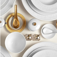 L'Objet Soie Tressée White Dinnerware, featuring elegant French plates and bowls with intricate patterns and gold accents, brings a luxurious touch to the table.